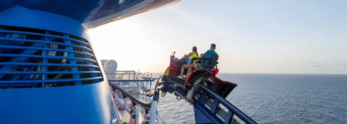 woman and man pass by the ship funnel while riding bolt roller coaster with a view of the ship deck and ocean ahead