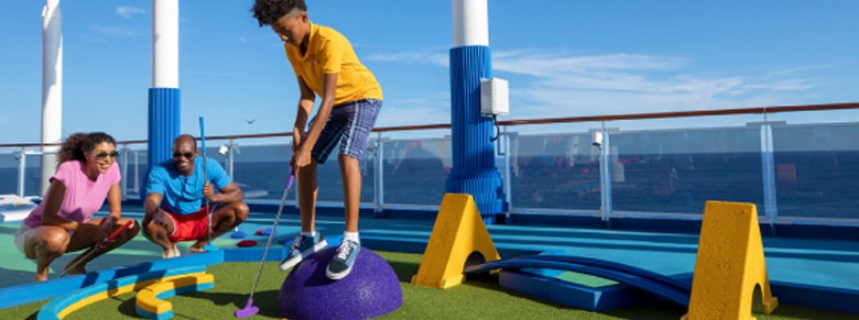 mother, father and son enjoy a game of mini golf on the outdoor deck with ocean in the background