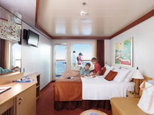 Two boys reading on a bed in a cruise ship cabin with an ocean view balcony.