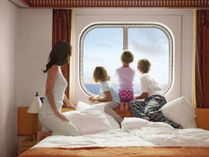 Family in pajamas looking out a large window in a cruise ship cabin.